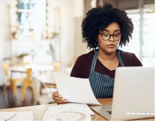 Business owner reviewing payroll paperwork at a laptop