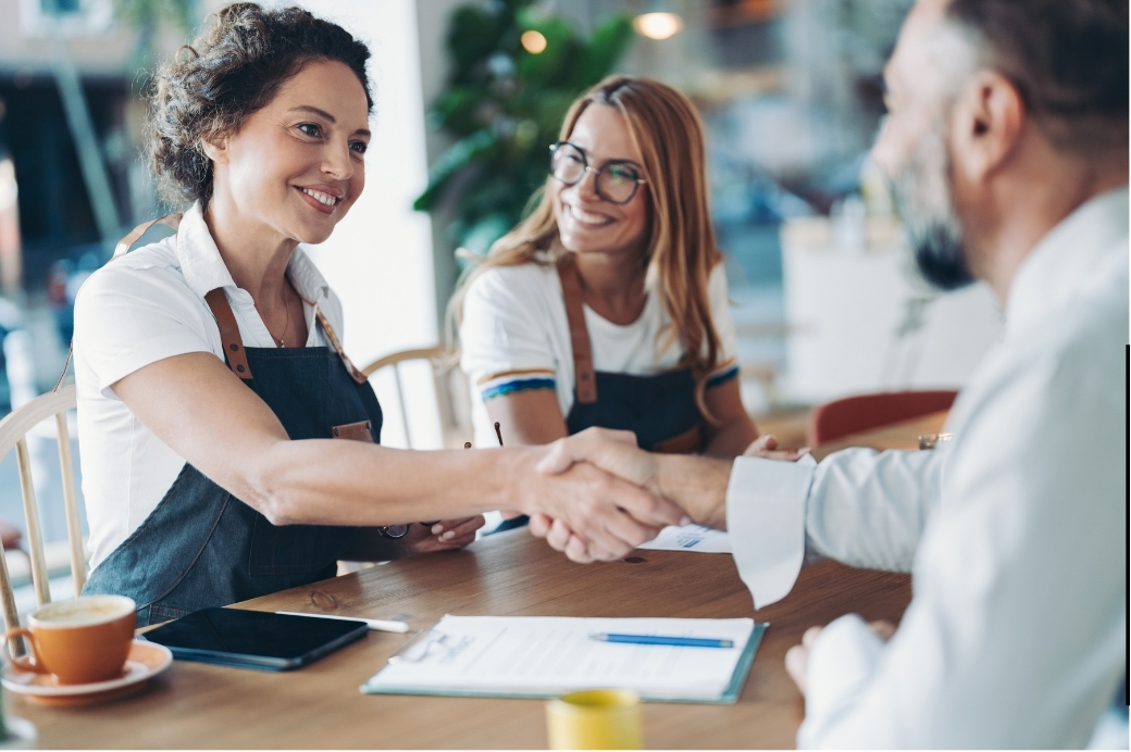 An AHEAD HR advisor shaking hands with two local business owners across a table